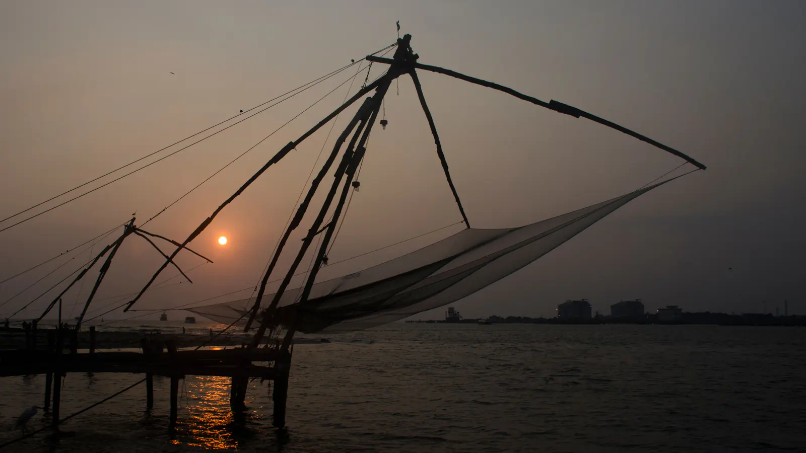 Chinese fishing nets silhouetted against an orange Fort Kochi sunset.